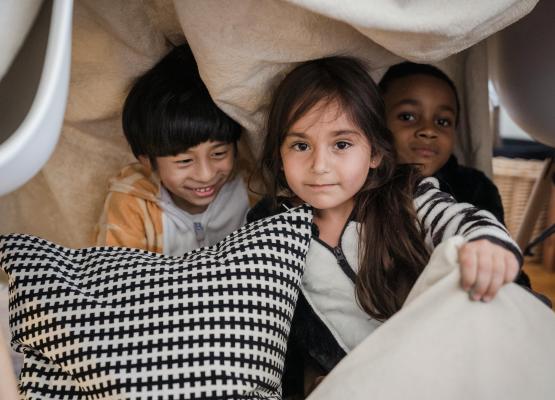 A girl and two boys play behind pillows