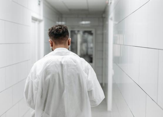 Back of man wearing white coat walking down hospital hallway.