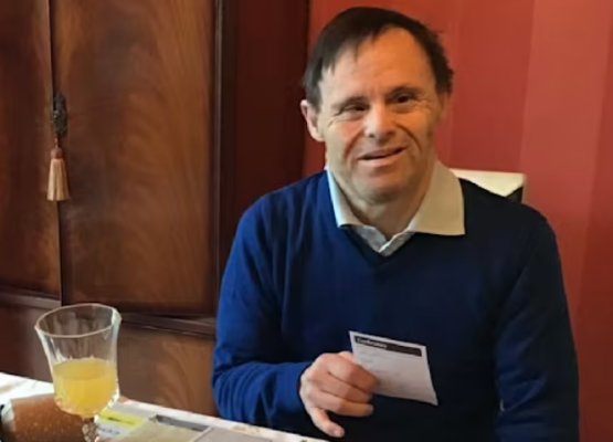 A man wearing a blue sweater sits at a table with a juice glass