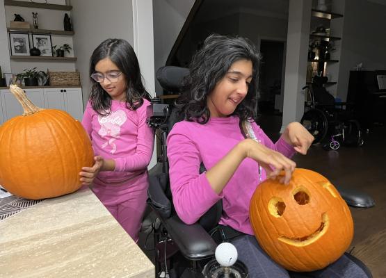Two girls with pink shirts carve pumpkins