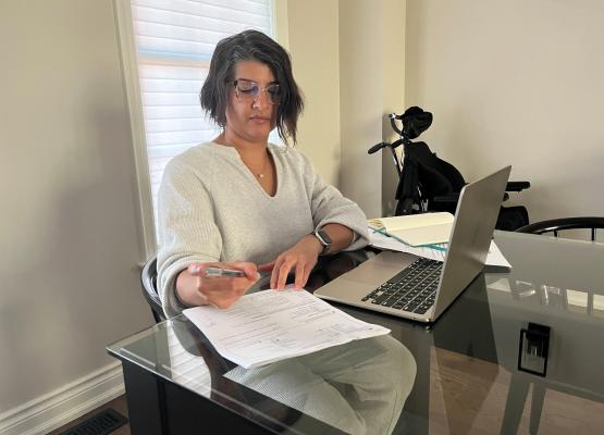 Woman with dark hair in front of laptop and papers.