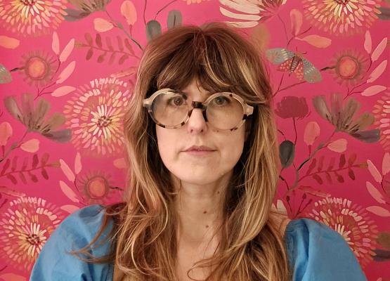 Woman with long hair and glasses against a pink wallpaper