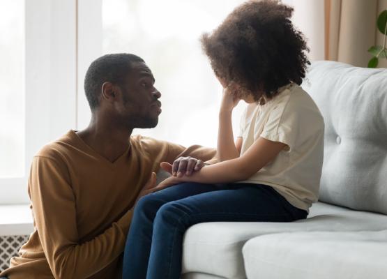 Young girl on couch being consoled by man.