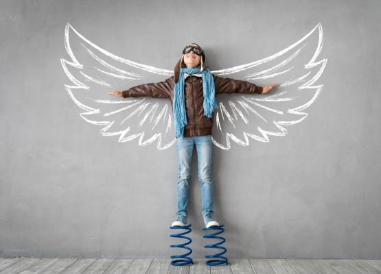 Boy stands on springs with arms spread on wall image of wings