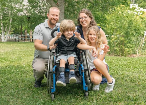 Boy outside in wheelchair beside girl with man and woman behind
