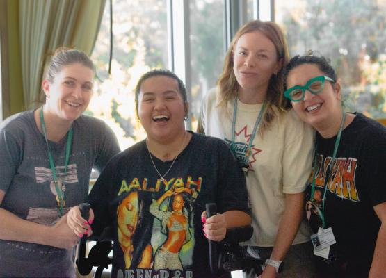 Teen wearing bright shirt and using walker surrounded by three women