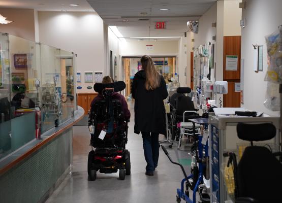 Young woman in wheelchair and woman with blonde hair walk through a hospital corridor