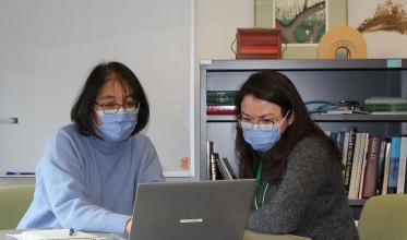 Two adults with mask on, looking at a laptop computer
