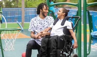 An adult is playing basketball with a teenager who is on a wheelchair