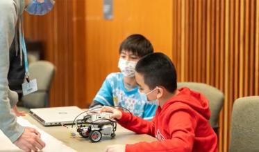 Two kids with mask on, playing Lego robotics