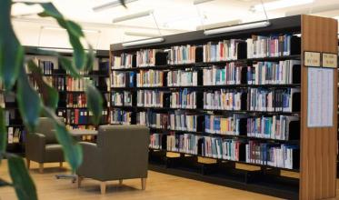 A coffee table with 2 chairs, in a library setting with some books on bookshelfs