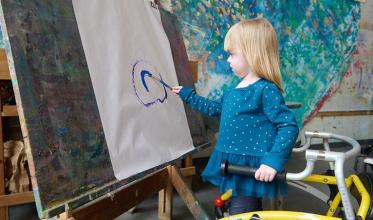 A child holding a wheelchair with one hand, and painting on the other hand