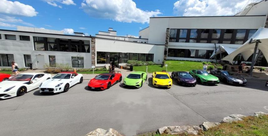 exotic cars lined up in front of a building, parked on concrete. Blue sky with clouds.