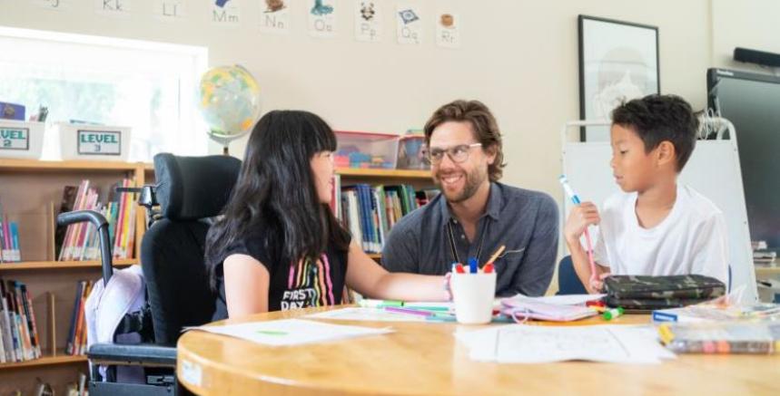 2 students and 1 teacher are seated at a classroom desk