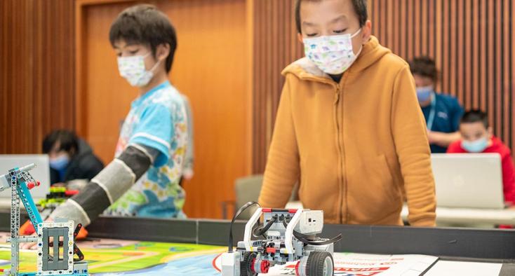 Two children with mask on playing some robotics games