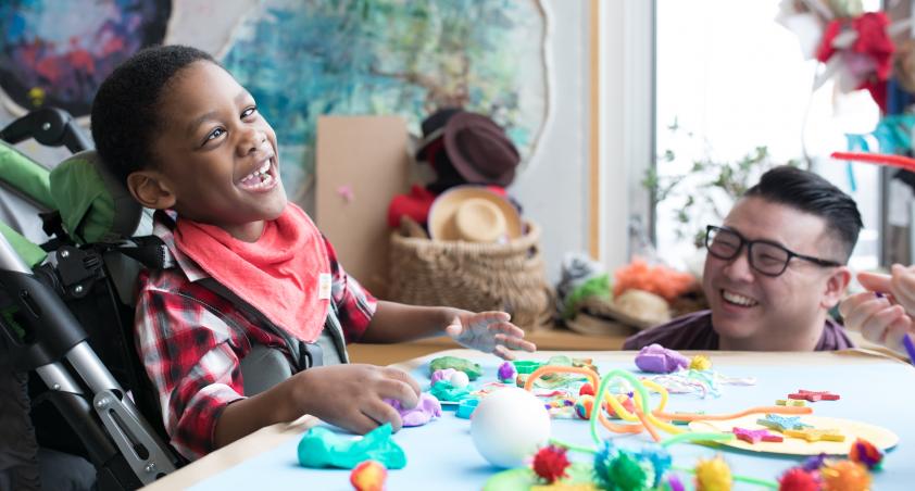 A little boy in a wheel chair playing with arts and crafts at a table