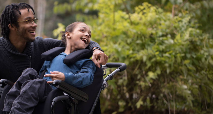 A young girl in a wheelchair and her father has his arm around her