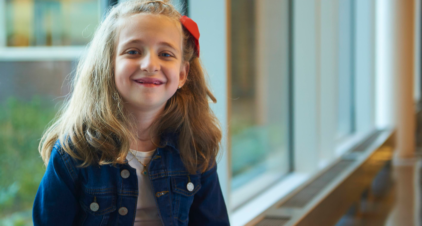 little girl with long blonde hair with a red bow in it wearing a jean jacket