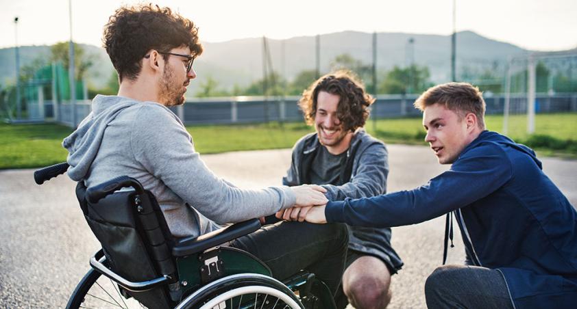 2 teenagers with another teenager on wheelchair playing in a playground