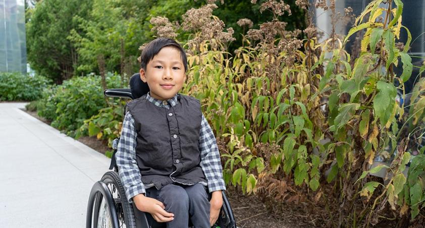 A young child sitting on a wheelchair, in a garden setting