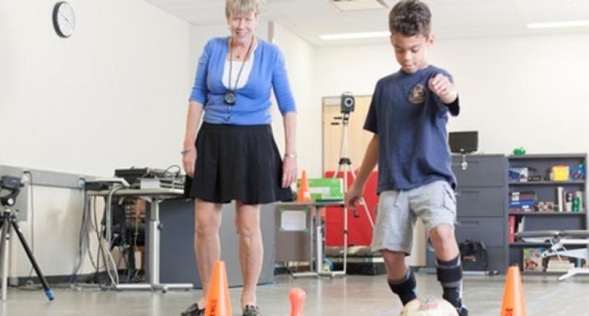 Child kicking a soccer ball with adult in background observing