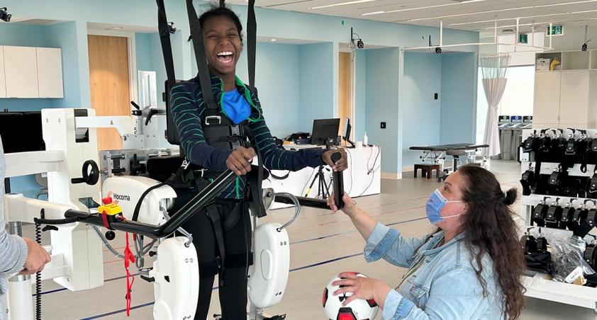 A child is using an equipment in an exercise room, being assisted by an adult