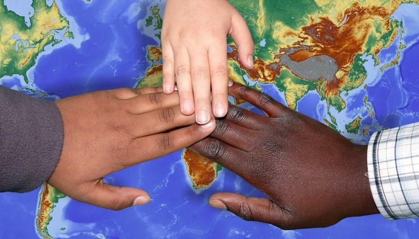 Three hands on top of one another, touching a picture of a world map