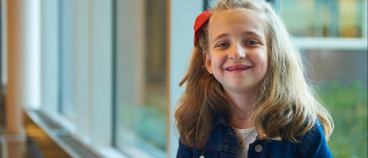 little girl with light skin tone and long blonde hair with a red bow in it wearing a jean jacket