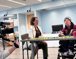 An adult and a teenager in a wheelchair are being interviewed by a TV station