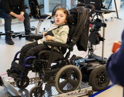 A child in a wheelchair, wearing a BCI headset, using a wheelchair trainer to move