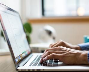 Adult typing on a keyboard by a window