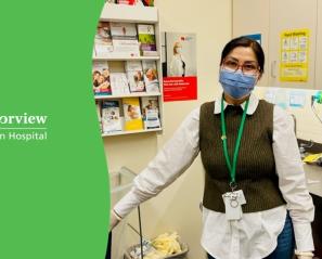 Rupinder wearing brown-rimmed glasses, a white shirt and a forest green sweater vest stands next to the Holland Bloorview logo on green background