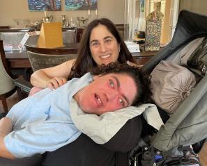 Young man with dark hair smiling in reclining wheelchair with woman with dark hair smiling behind
