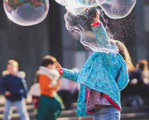 young child wearing blue jacket plays with bubbles 