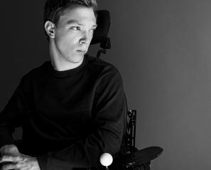 A young adult with light skin tone and short hair who uses a wheelchair.
