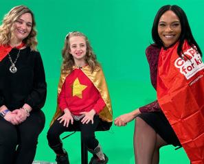 Two adults and a child with their red capes sitting in front of a green background for TV airing