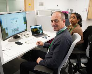 Two adults sitting in front of some computers, facing the camera