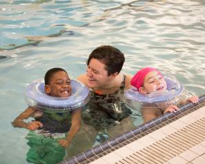 Two young kids at pool's edge with an adult