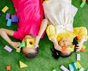 Two young children lie on the floor and play with blocks