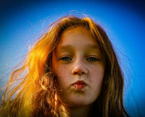 Girl with red hair purses lips on blue background