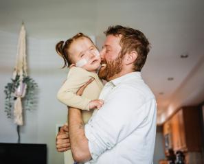 Man with beard hugs small girl with pony tails and nasal prongs
