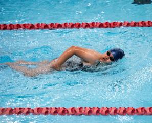 Woman in blue cap and black goggles swims the front crawl in a pool lane with red dividers