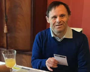 A man wearing a blue sweater sits at a table with a juice glass