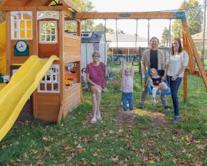 Young child wearing oxygen prongs in a swing beside a girl hanging from a bar with three adults in the background