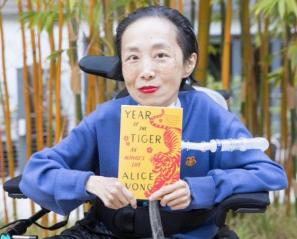 Woman in royal blue holding book called Year of the Tiger sits in wheelchair