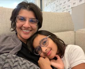 Woman with dark hair and glasses snuggles with girl with dark hair and glasses