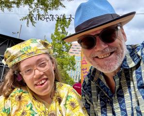 Girl with yellow sunflower hat and shirt smiles with man with blue brimmed hat and sun glasses