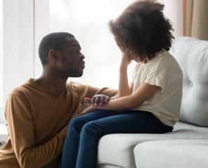Young girl on couch being consoled by man.