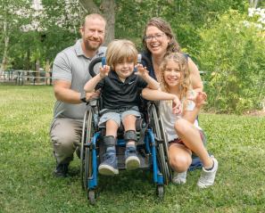 Boy outside in wheelchair beside girl with man and woman behind