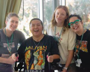 Teen wearing bright shirt and using walker surrounded by three women